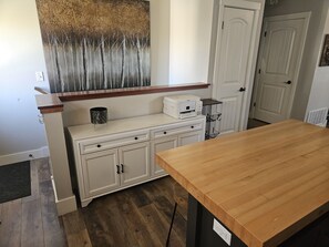 Ein Zimmer mit Holztisch, weißen Schränken, einem Drucker und einem großen abstrakten Gemälde an der Wand.