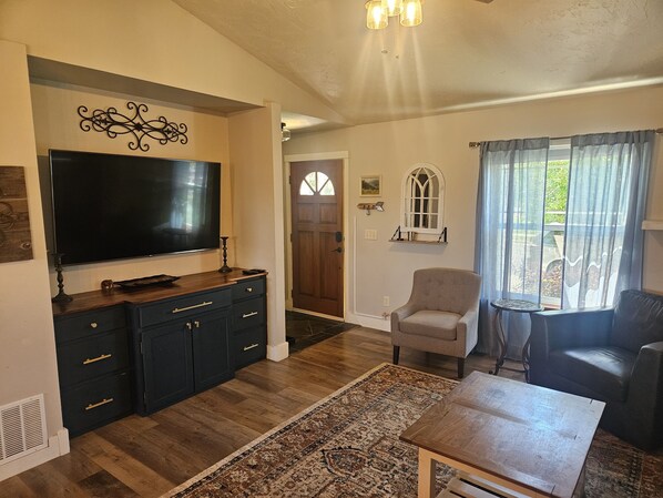 A living room with a flat-screen TV, dark wooden cabinets, a beige armchair, a round coffee table, and a patterned rug. - Sunny Threshold
Spacious 4-bedroom house in quaint Helena with cool AC (Helena)