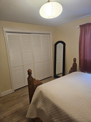 Ein Schlafzimmer mit Bett, Kleiderschrank, Spiegel und Deckenleuchte.