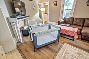 A living room with a baby playpen, a leather sofa, a TV, and a fireplace. - Walnut Porch! Cozy Historic Home Near OCC (Colorado Springs)