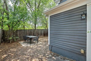A backyard with a patio table and chairs, a wooden fence, and a house with grey siding. - Walnut Porch! Cozy Historic Home Near OCC (Colorado Springs)