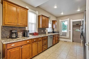 A kitchen with wooden cabinets, a granite countertop, a coffee maker, and a dishwasher. - Walnut Porch! Cozy Historic Home Near OCC (Colorado Springs)