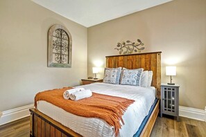 A hotel room with a wooden bed, two bedside tables with lamps, a decorative wall piece, and a window with a metal design. - Walnut Porch! Cozy Historic Home Near OCC (Colorado Springs)