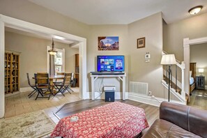 A living room with a fireplace, a television, and a dining area with chairs and a table. - Walnut Porch! Cozy Historic Home Near OCC (Colorado Springs)