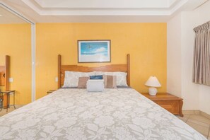 Une chambre d’hôtel avec un grand lit, une table de chevet avec une lampe, un tableau encadré au mur et une fenêtre avec des rideaux.