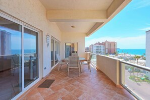 Ein Balkon mit Tisch und Stühlen, eine Schiebetür aus Glas und Blick auf das Meer und Gebäude.