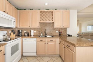 Une cuisine avec des meubles de couleur bois clair, un plan de travail en granit, un évier en acier inoxydable, un four à micro-ondes, une cuisinière et un lave-vaisselle.