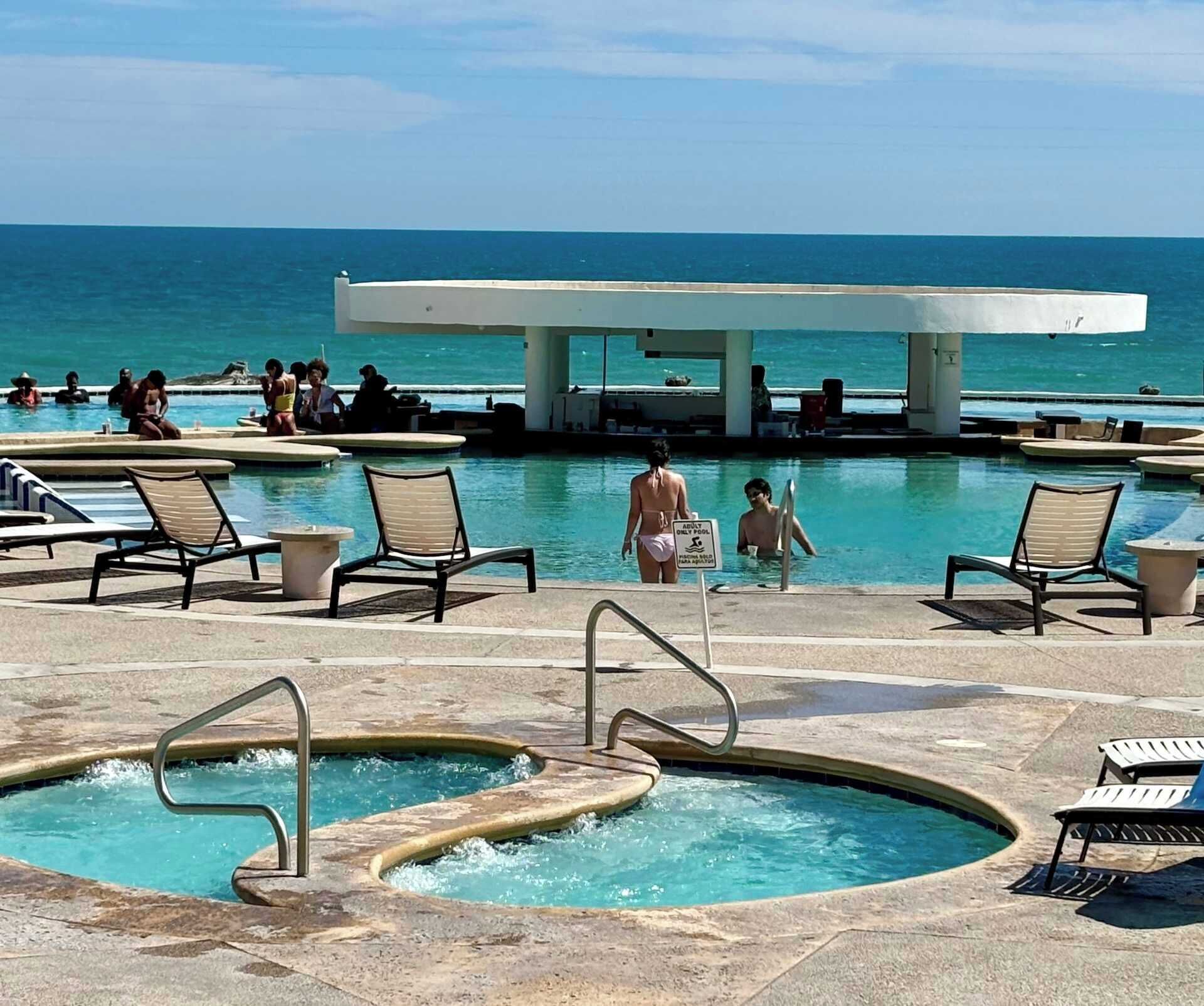 Ein Poolbereich mit Liegestühlen und einem Whirlpool mit Blick aufs Meer.