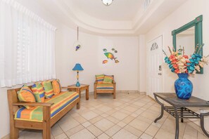 Ein Zimmer mit einer Holzsofa, einem kleinen Tisch, einem Stuhl, einer Lampe und einer Vase mit Blumen.