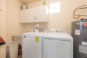 A laundry area with two front-loading washing machines, a metal water heater, and a metal bucket on the wall.