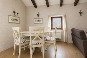 A dining area with a round table and four chairs, a window with curtains, and a sofa.