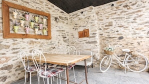 A rustic stone wall with a wooden table and metal chairs, a bicycle, and a wall-mounted planter with flowers. - Schist Houses - Casa da Capela (2-Bedroom House) (Bragança)