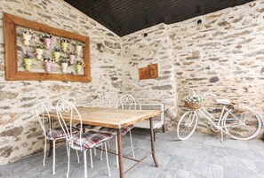 Eine rustikale Steinmauer mit einem Holztisch und Metallstühlen, einem Fahrrad und einem wandmontierten Blumenkasten.