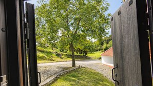 An open door revealing a cobblestone path, a tree, and a white building with a red roof.