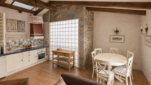 A rustic kitchen with stone walls, wooden beams, a tiled backsplash, and a dining area with a round table and chairs.