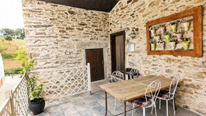 A stone-walled outdoor seating area with a wooden table and metal chairs, a potted plant, and a wall-mounted flower display.