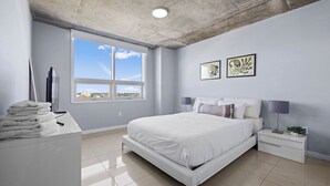 Un dormitorio con una cama grande, una mesita de noche, un escritorio con lámpara y una obra de arte en la pared.