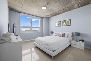 A bedroom with a large bed, a nightstand, a desk with a lamp, and artwork on the wall. - Top Modern 2BR in Miami - Best location ever! (Miami)