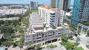 Un edificio de varios pisos con jardín en la azotea, rodeado de otros edificios altos y vegetación.