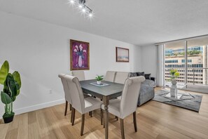A modern living room with a dining area, large windows, and a view of a building. - Stylish Brickell Apartment • Sleeps 6•Free Parking (Miami)