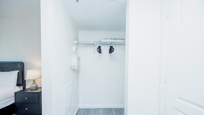 Un dormitorio con cama, mesita de noche, lámpara y perchero con ropa colgada.