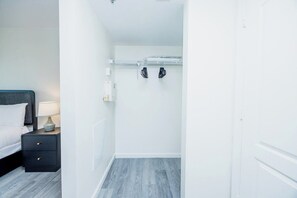 A bedroom with a bed, nightstand, lamp, and a coat rack with hanging items. - Brickell brand new unit 26th floor (Miami)
