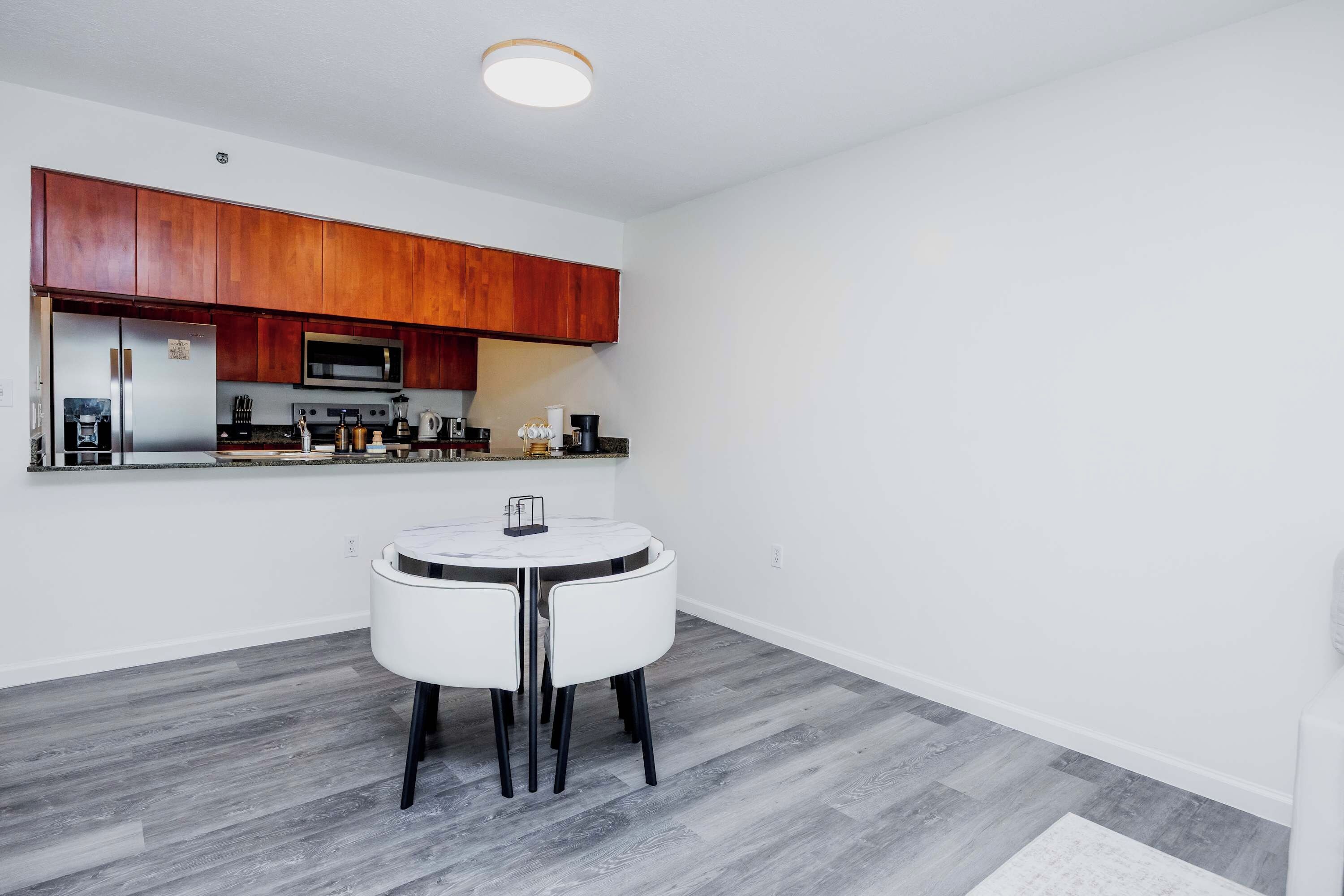 A compact kitchen with wooden cabinets, a built-in oven, and a round dining table with chairs.