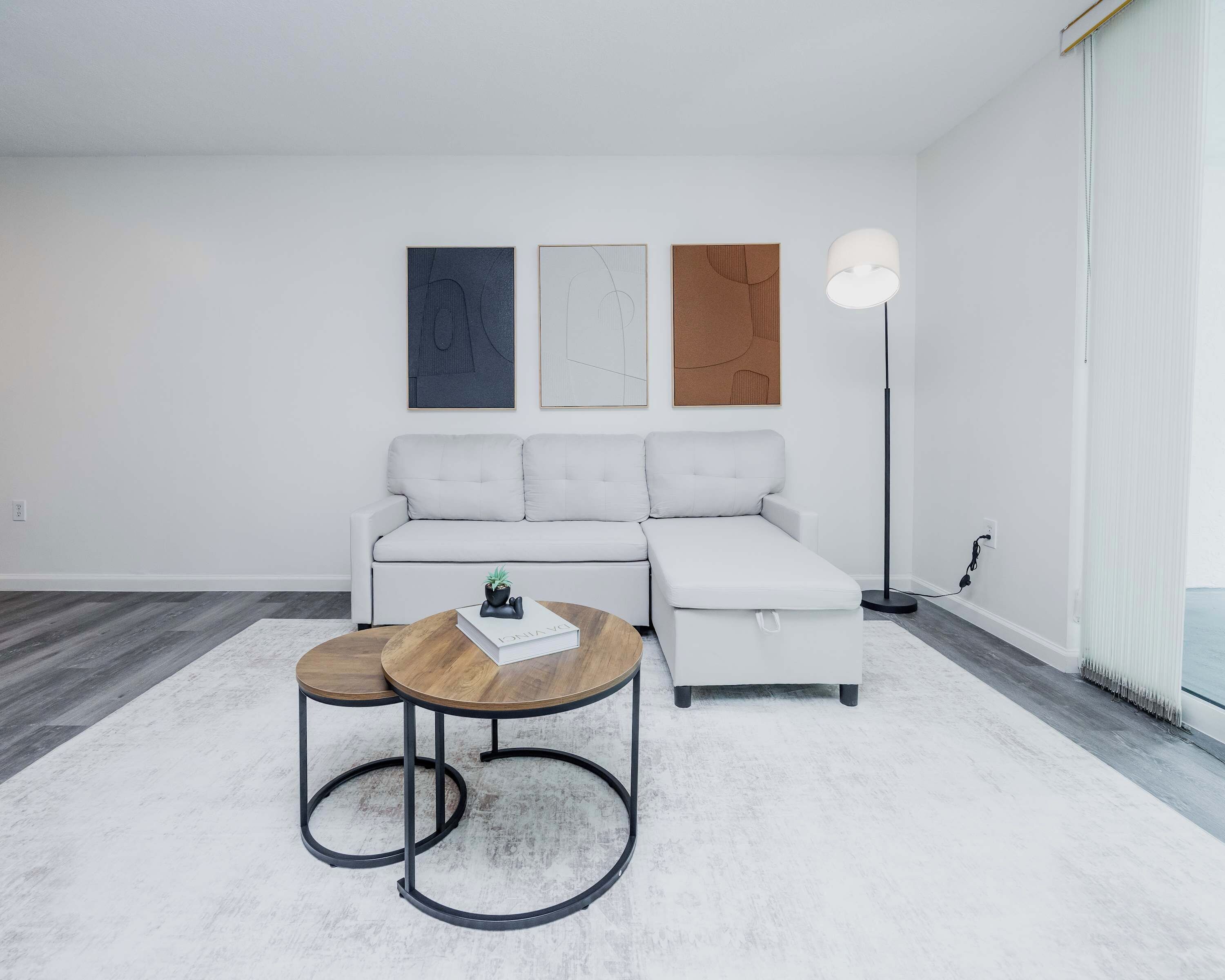 A modern living room with a sectional sofa, two round tables, and three framed artworks on the wall.