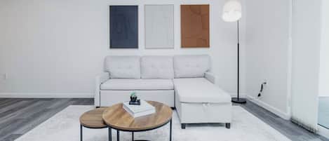 Un salon moderne avec un canapé d’angle, deux tables rondes et trois œuvres d’art encadrées accrochées au mur.