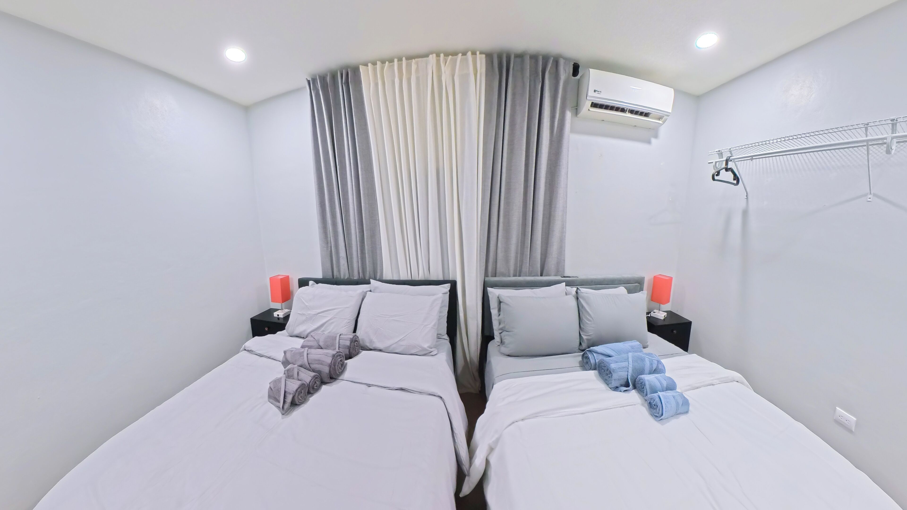 A hotel room with two beds, a ceiling fan, an air conditioning unit, and a window with curtains.