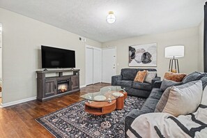 A living room with a flat-screen TV, fireplace, sofa, and a coffee table with glass top. - The Mod Maze | 2 Kings • Fireplace • Central OMAHA (Omaha)