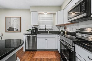 A modern kitchen with white cabinets, stainless steel appliances, a black countertop, and a wooden floor. - The Mod Maze | 2 Kings • Fireplace • Central OMAHA (Omaha)