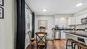 A modern kitchen with white cabinets, a wooden dining table, and bar stools. - The Mod Maze | 2 Kings • Fireplace • Central OMAHA (Omaha)