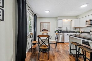 A modern kitchen with white cabinets, a wooden dining table, and bar stools. - The Mod Maze | 2 Kings • Fireplace • Central OMAHA (Omaha)