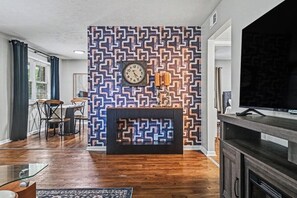 A living room with a patterned wall, a fireplace, a dining area, and a television. - The Mod Maze | 2 Kings • Fireplace • Central OMAHA (Omaha)