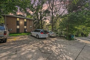 A parking area with two cars, a brick building, and trees. - The Mod Maze | 2 Kings • Fireplace • Central OMAHA (Omaha)