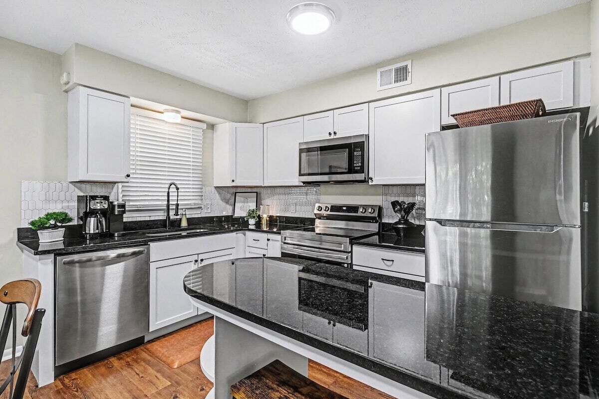 A modern kitchen with stainless steel appliances, white cabinetry, and a black countertop.