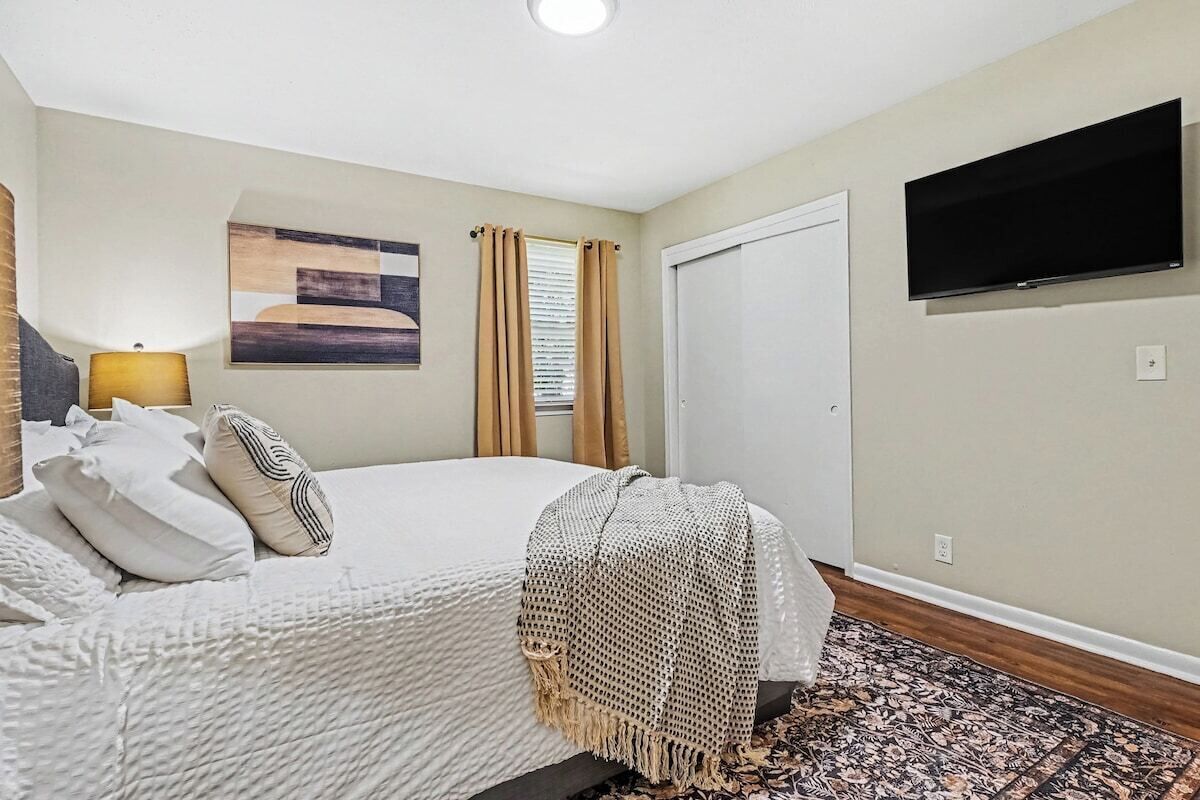 A bedroom with a bed, a television mounted on the wall, and a patterned rug.