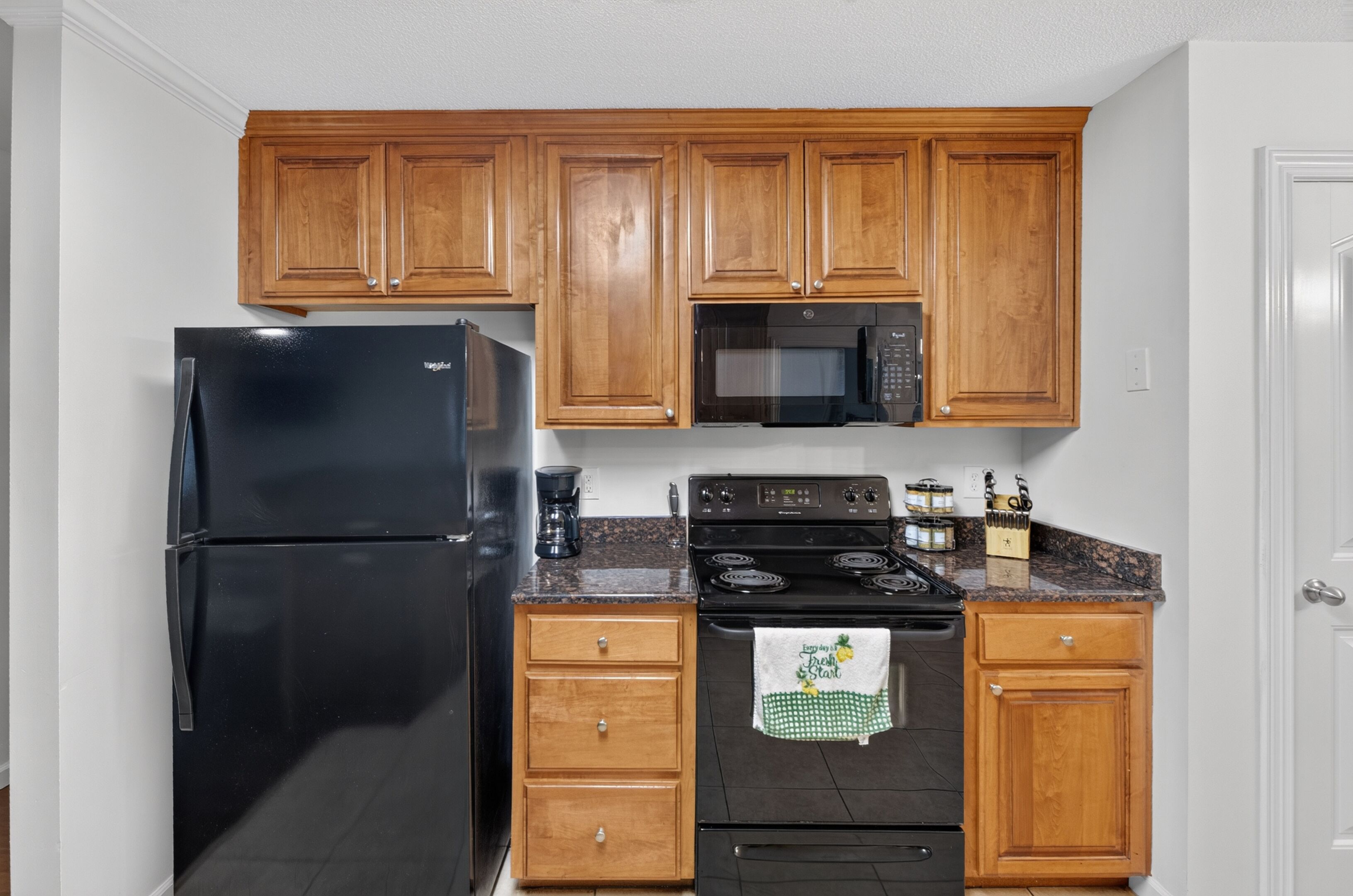 Una cocina con armarios de madera, un refrigerador negro, microondas, estufa y cafetera.