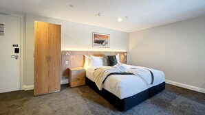 Ein Hotelzimmer mit einem Bett, einem Holzschrank, einem Nachttisch und einem an der Wand hängenden Bild.