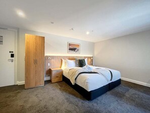 A hotel room with a bed, a wooden wardrobe, a nightstand, and a wall-mounted picture. - Above the Lake | Studio Escape (Queenstown)