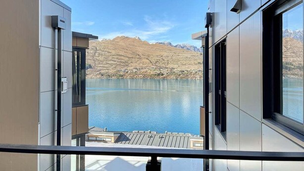 Ein modernes Gebäude mit großen Fenstern mit Blick auf einen ruhigen See und Berge.