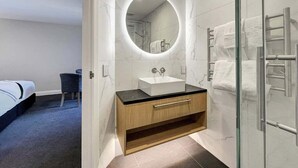 Ein modernes Badezimmer mit Duschkabine aus Glas, einem runden Spiegel und einem Holzwaschtisch mit Waschbecken.