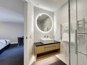 A modern bathroom with a glass shower enclosure, a round mirror, and a wooden vanity with a sink. - Above the Lake | Studio Escape (Queenstown)