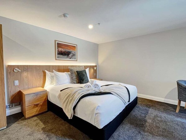 A modern bedroom with a large bed, a nightstand, a chair, and a painting on the wall. - Above the Lake | Studio Escape (Queenstown)