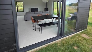 A modern house with a sliding glass door leading to an open-plan living area featuring a dining table, chairs, and a sofa. - Come and enjoy some rural views in awesome Taupo (Kinloch)