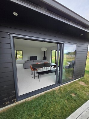 Ein modernes Haus mit einer Schiebeglastür, die zu einem offenen Wohnbereich führt, der einen Esstisch, Stühle und ein Sofa beinhaltet.