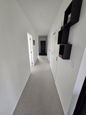 A hallway with white walls, a carpeted floor, and black shelves on the right. - Come and enjoy some rural views in awesome Taupo (Kinloch)