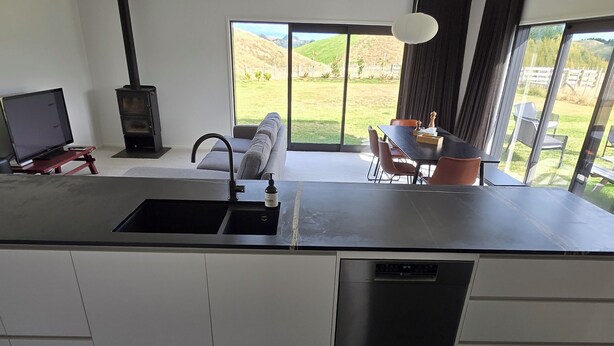 A modern kitchen with a built-in dishwasher, a large window overlooking a grassy yard, and a dining area with a table and chairs. - Come and enjoy some rural views in awesome Taupo (Kinloch)