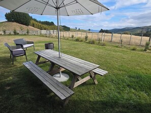 A wooden picnic table with benches and a white umbrella in a grassy outdoor area. - Come and enjoy some rural views in awesome Taupo (Kinloch)
